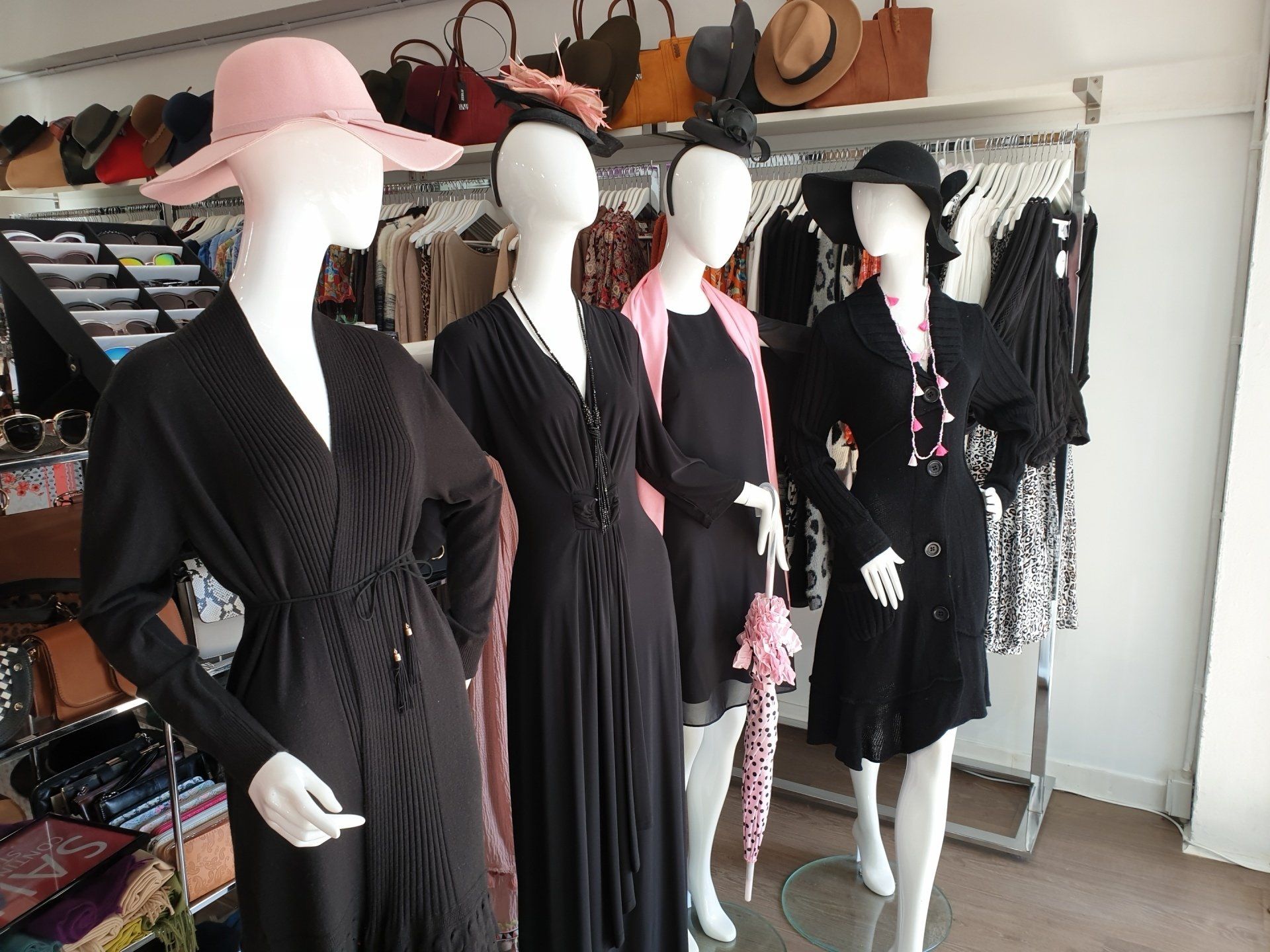 Four mannequins in a clothing store display.  They wear black dresses and hats.  Pink accessories are featured.