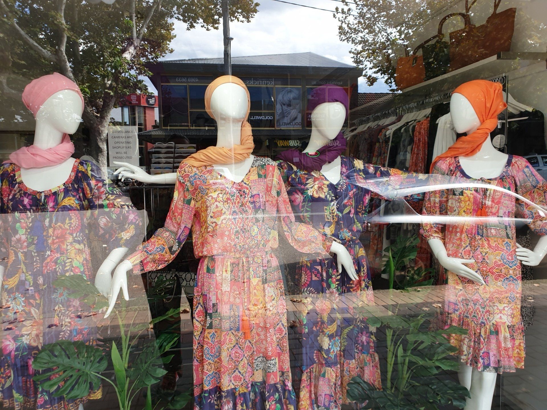 Window display featuring mannequins wearing colorful floral dresses and headscarves.