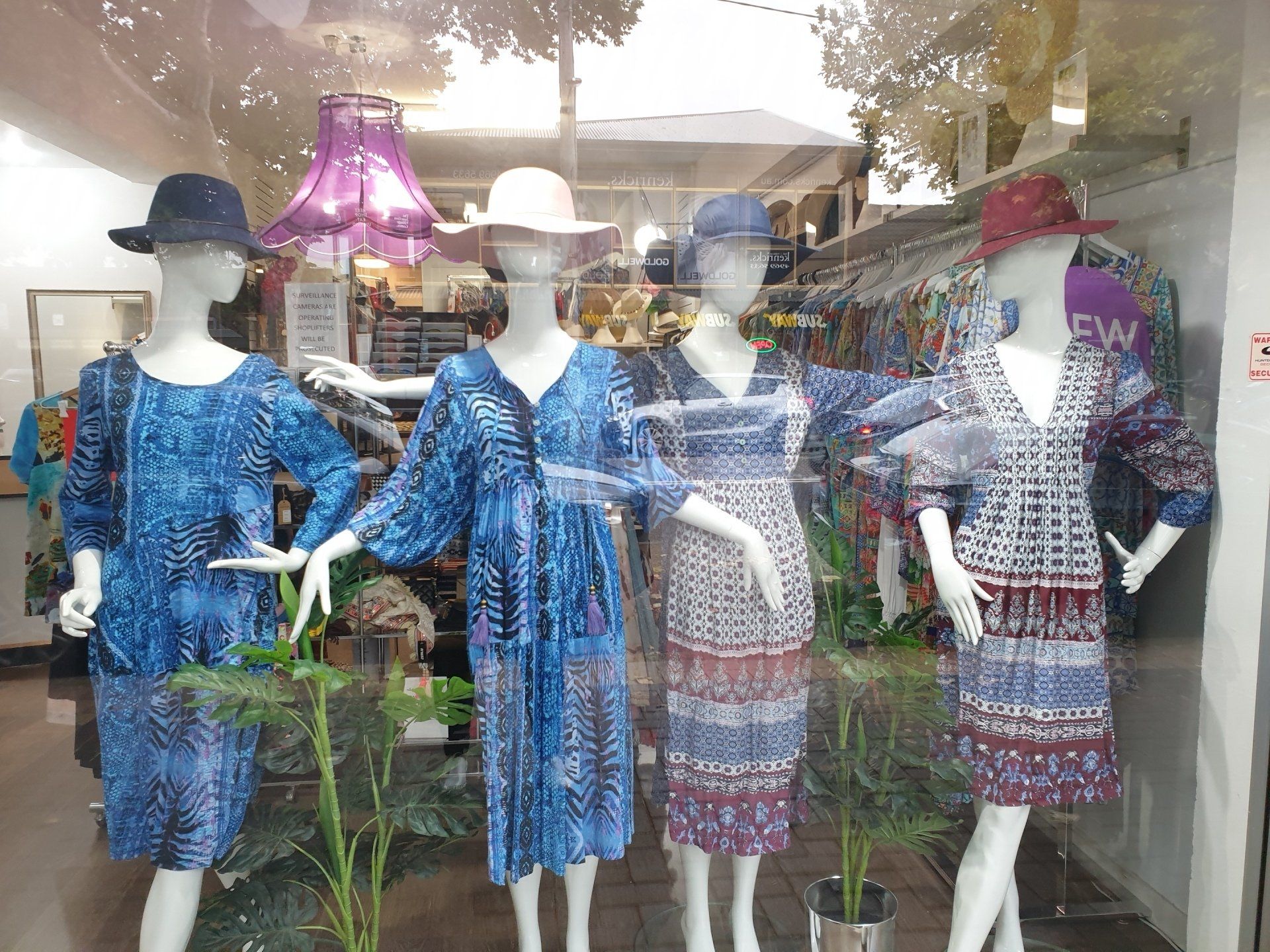 Four mannequins in a shop window wearing blue patterned dresses and hats; store interior visible.