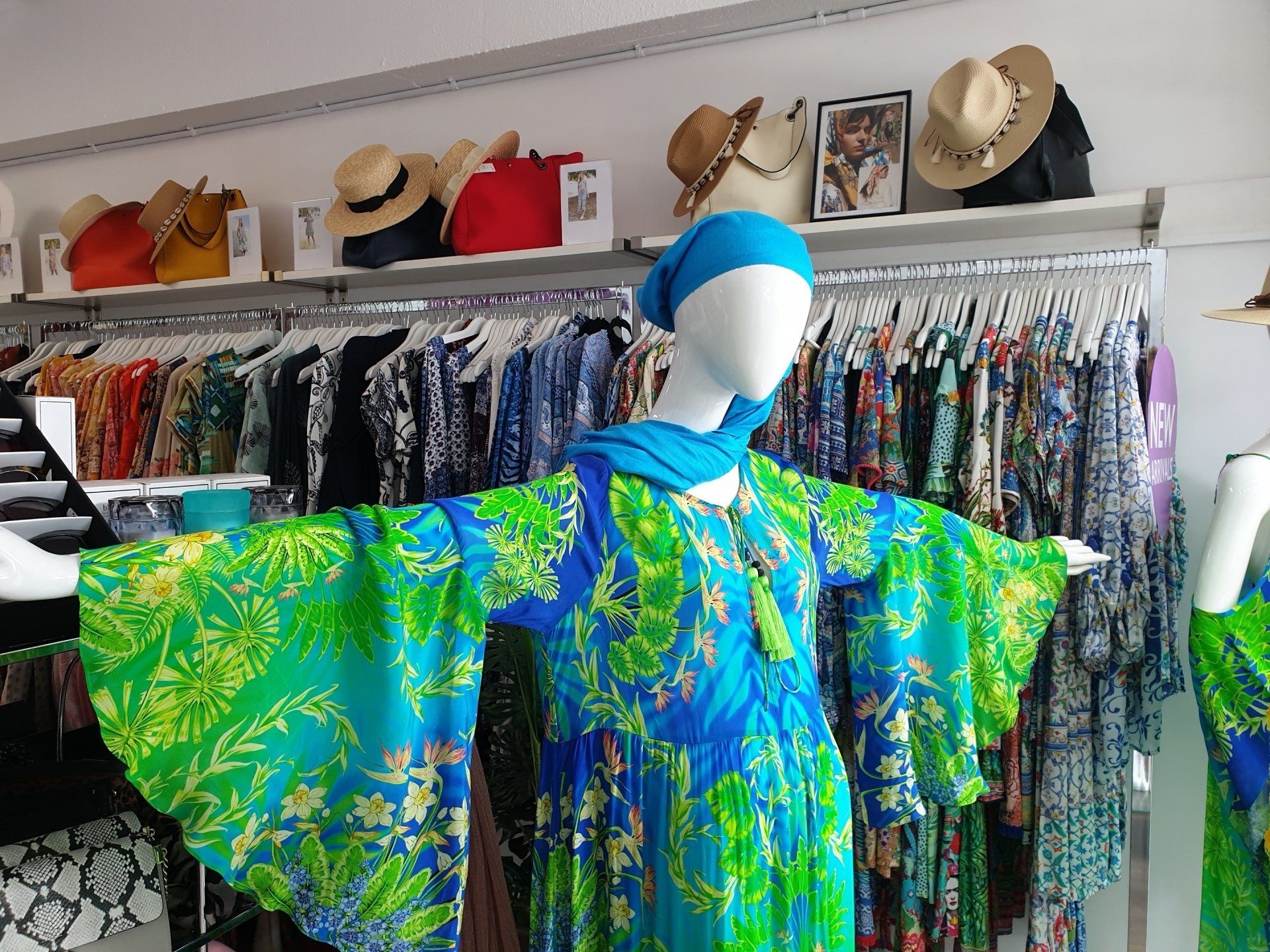 Mannequin in blue and green patterned dress, arms outstretched, in a clothing store.