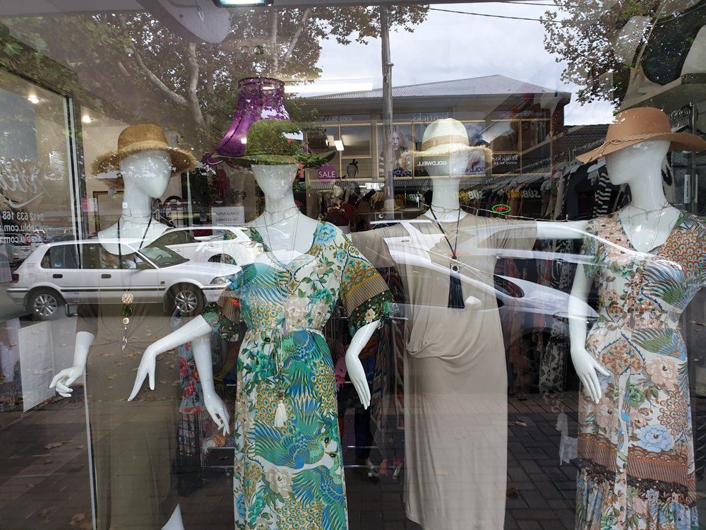 Storefront display of mannequins wearing hats and summer dresses.