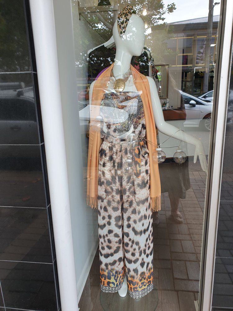 Mannequin in leopard print jumpsuit, necklace, and orange scarf in shop window.