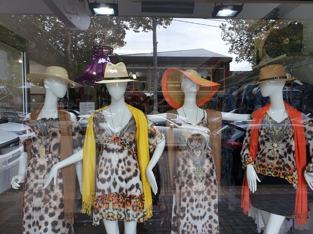 Four mannequins wearing leopard print dresses, hats, and colorful shawls in a shop window.