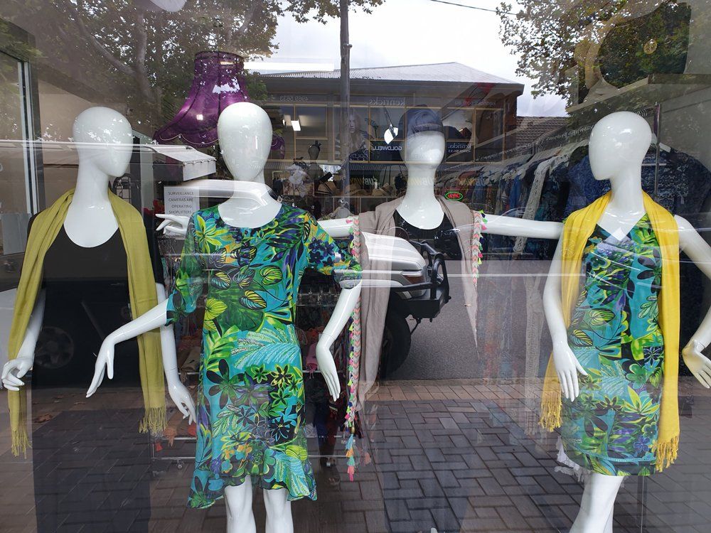 Four mannequins in a shop window display dresses in bright colors; yellow, green and teal.