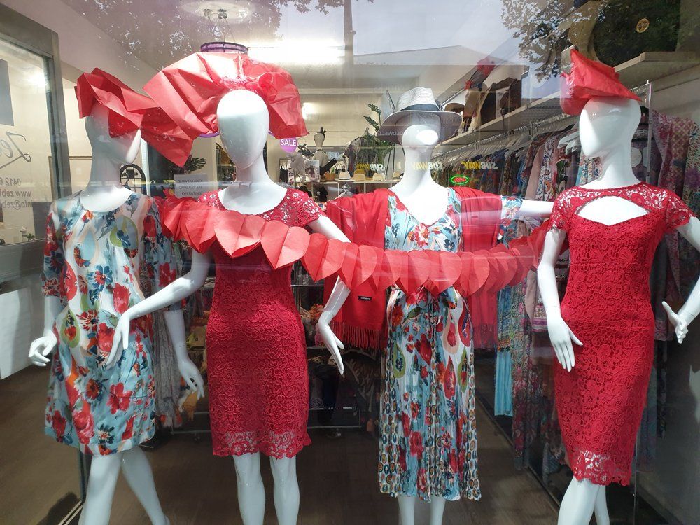 Window display with mannequins in red dresses, floral prints.