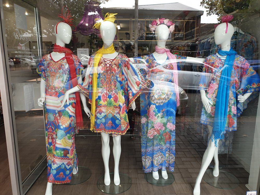 Four mannequins in a shop window wearing colorful patterned dresses and scarves.
