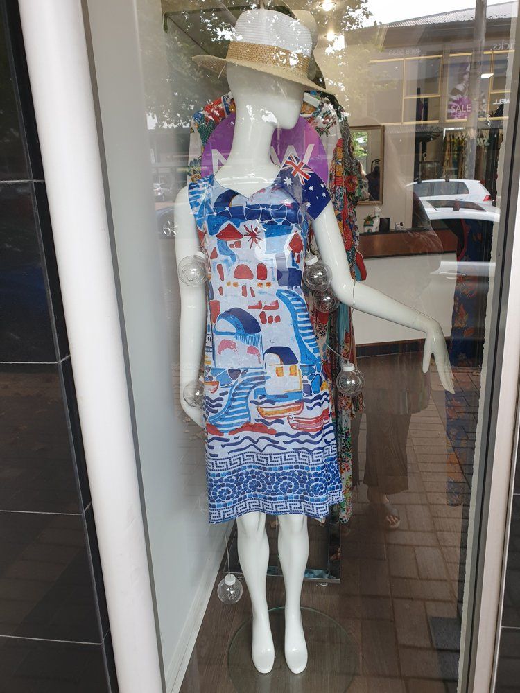 Mannequin in a shop window wears a blue and white print dress and straw hat.