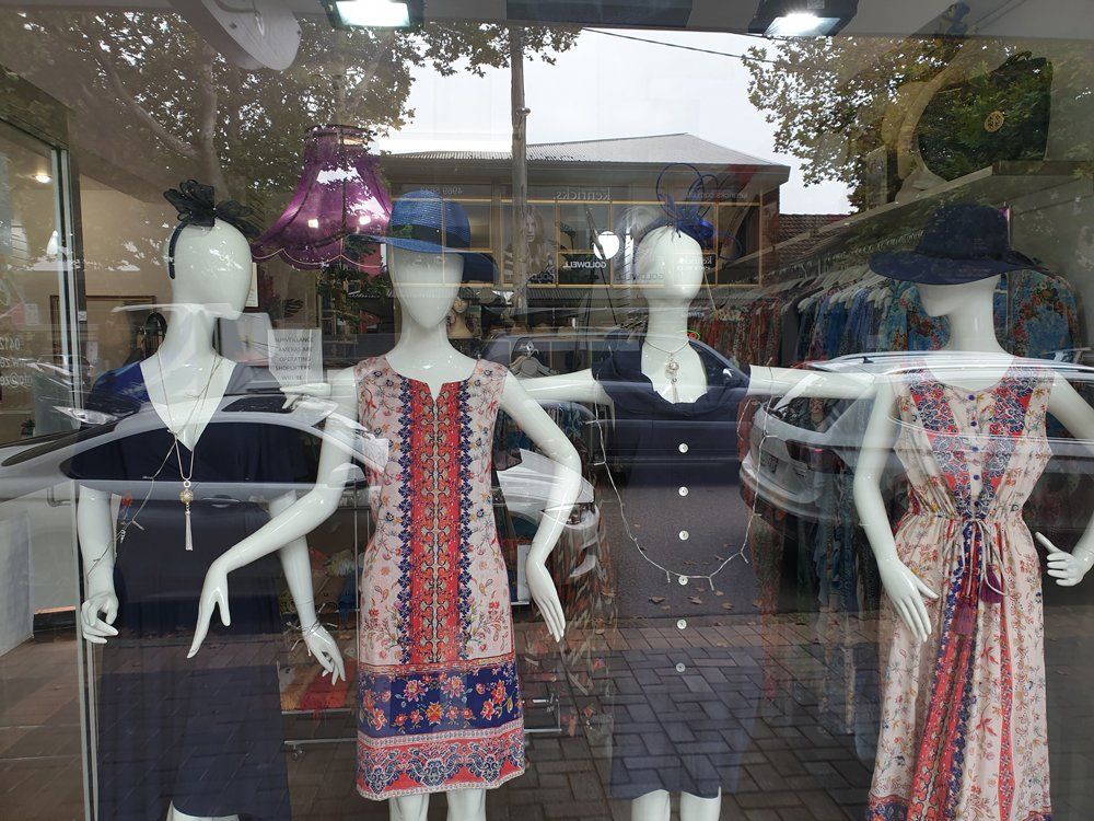 Mannequins in a shop window display dresses; blues, reds, and floral patterns.