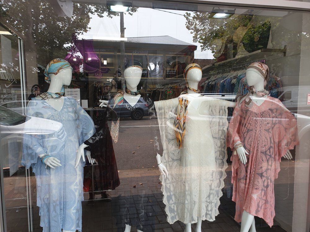 Four mannequins in a storefront window, wearing colorful vintage-style dresses and headscarves.