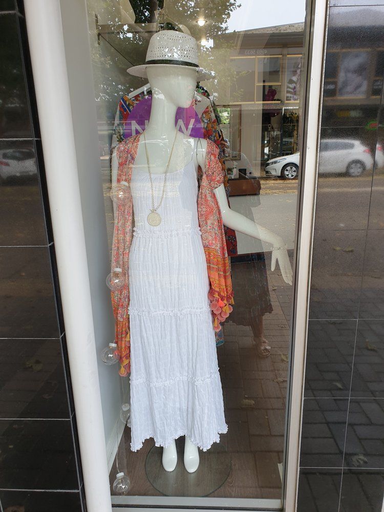 Mannequin in a shop window wearing a white dress, hat, and orange shawl.