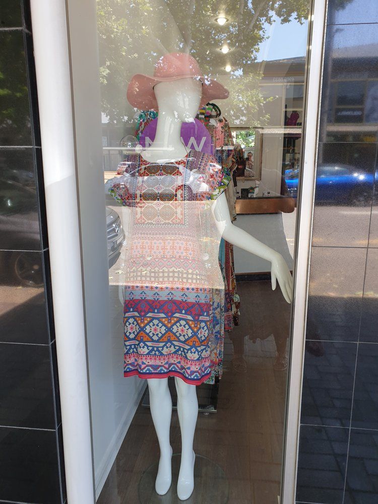 Mannequin wearing colorful dress and hat in a shop window.