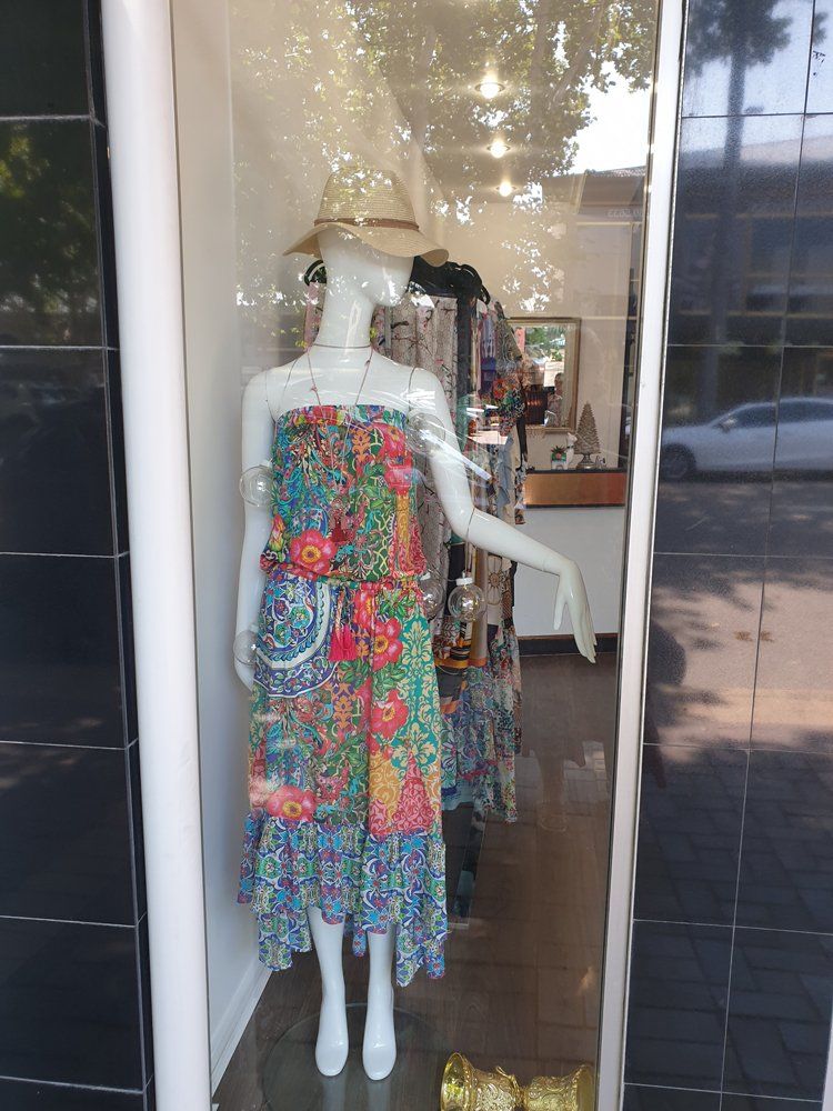 Mannequin in colorful floral print dress, wearing a hat, in a shop window.