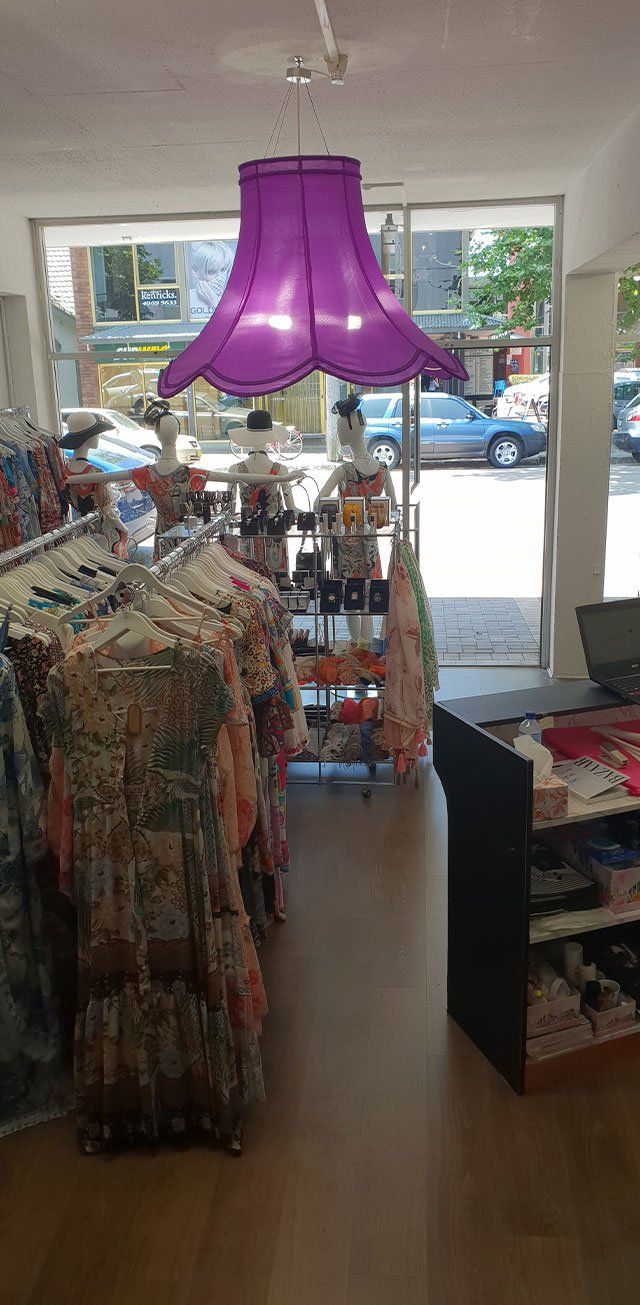 A retail store interior with a purple lampshade hanging above, clothes on display and a window view.