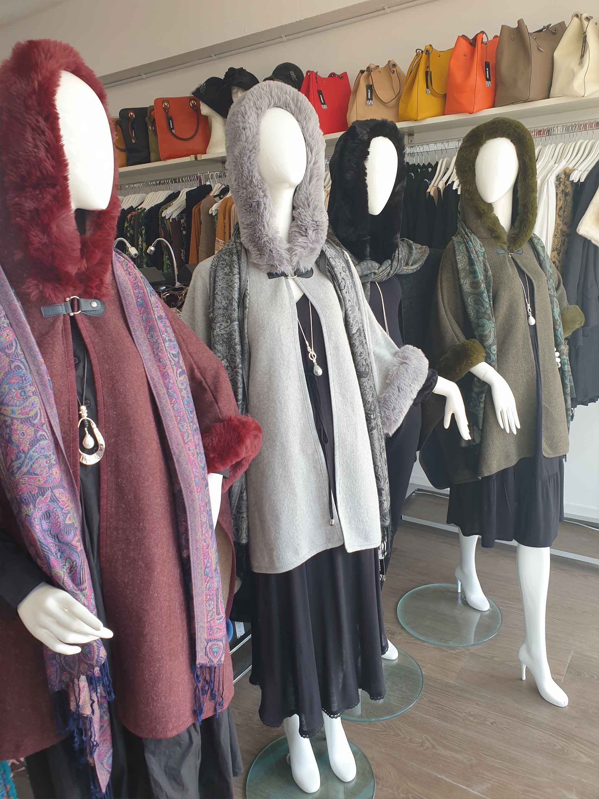 Mannequins in hooded capes with scarves, displayed in a shop.