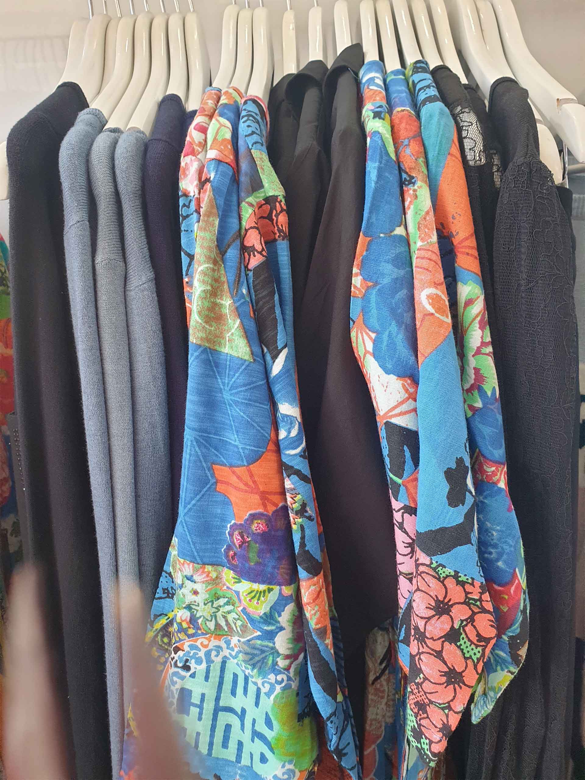 Clothes hanging on white hangers; focus on blue and orange patterned scarves.