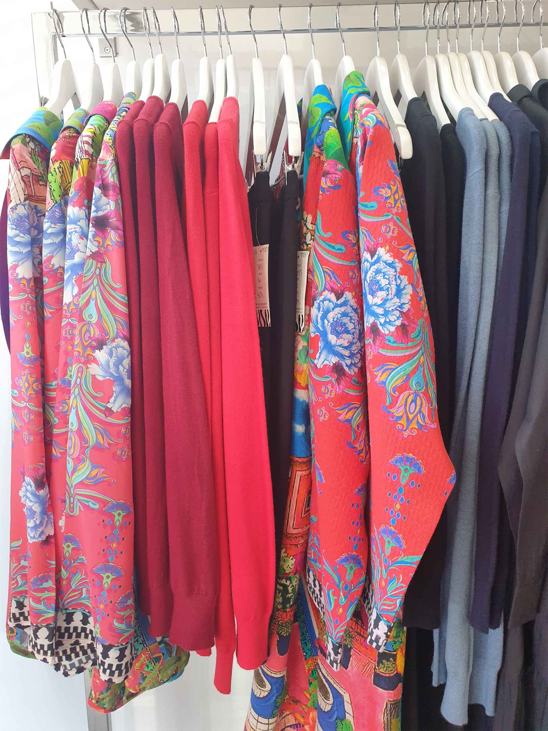 Clothes hanging on a rack; vibrant floral prints, red sweaters, and various dark colors.