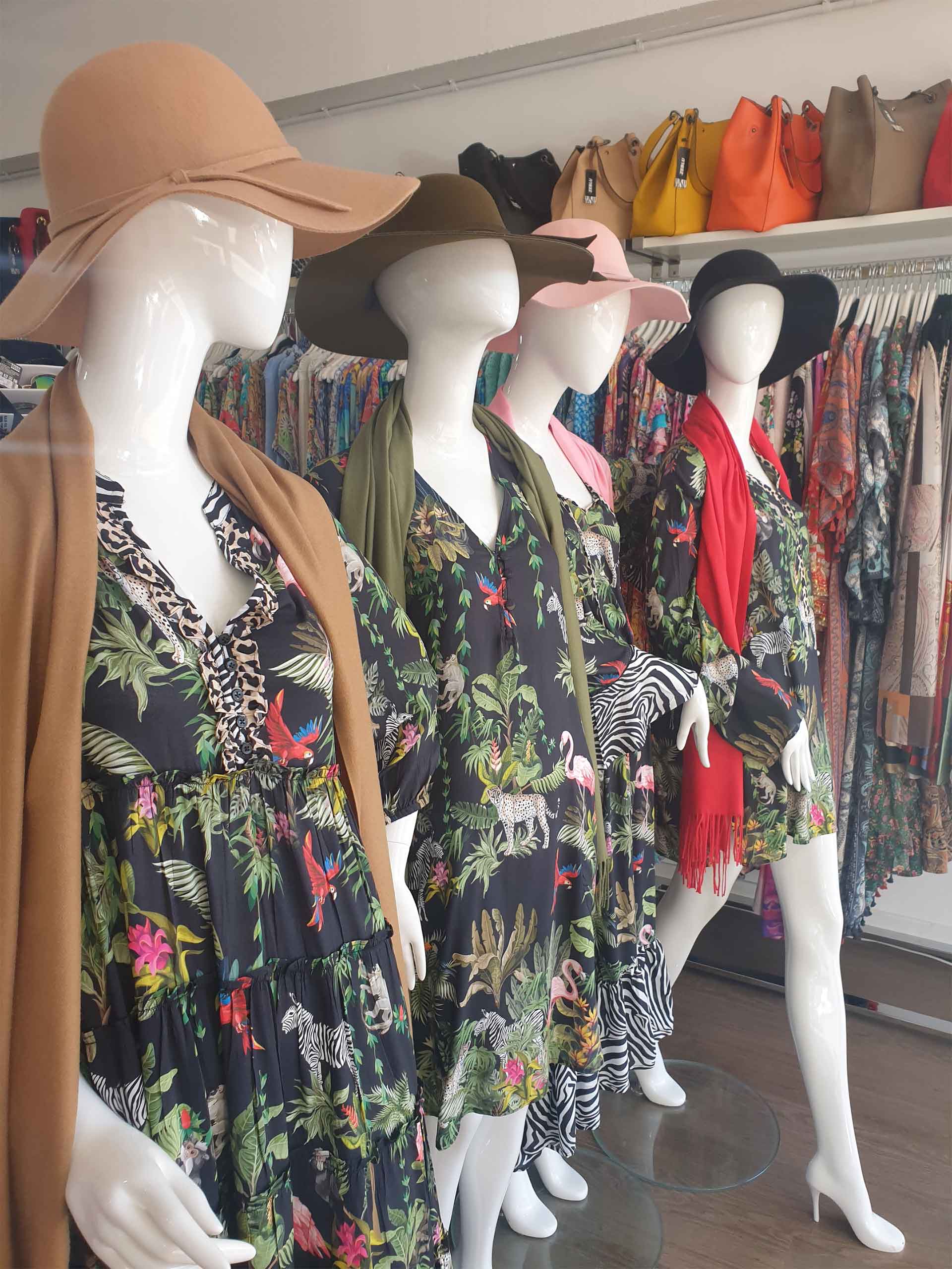 Mannequins in a clothing store wearing floral dresses, wide-brimmed hats, and accessories.