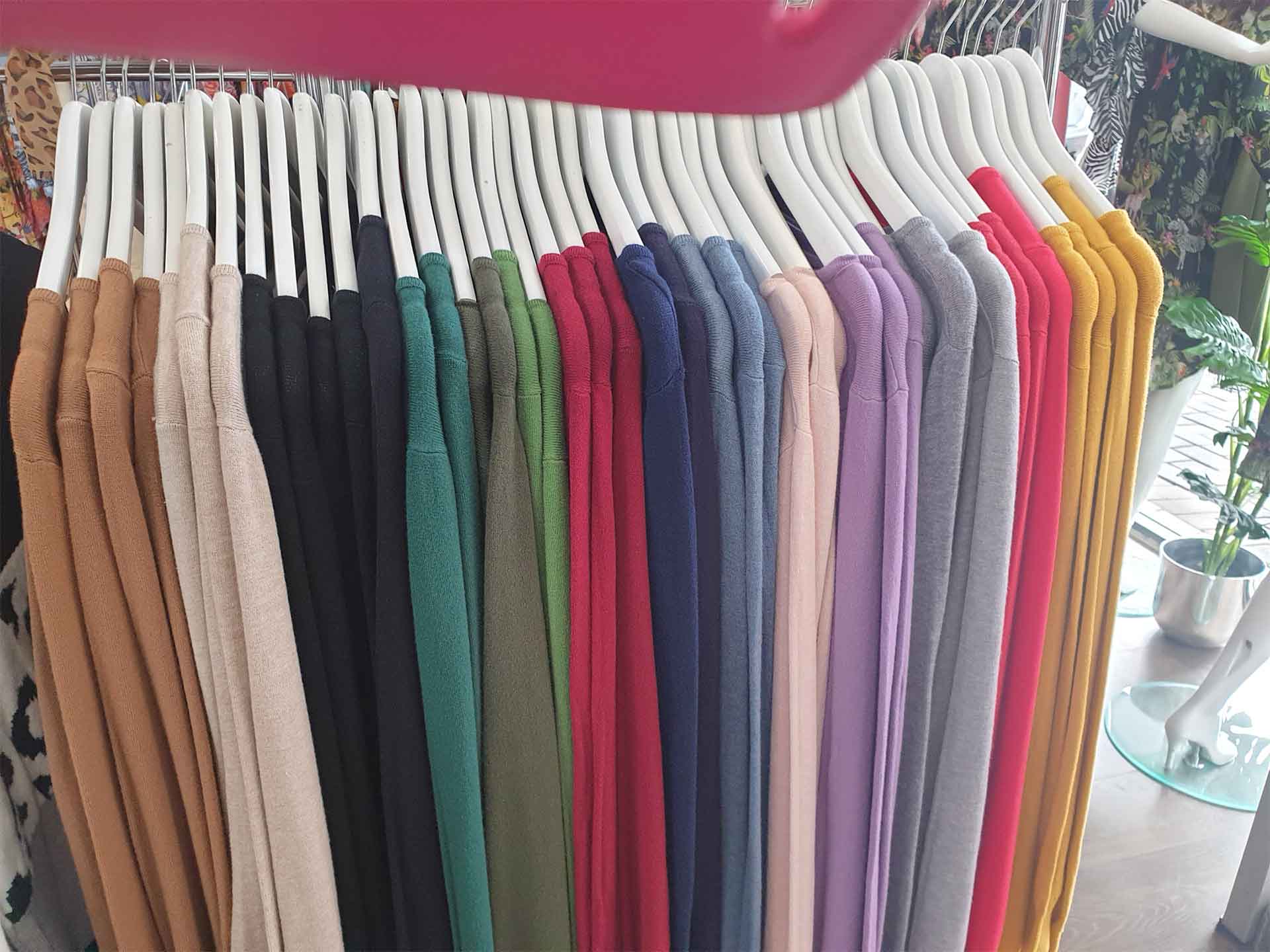 Clothing rack with rows of colorful pants, including shades of brown, black, green, red, blue, purple, gray, and yellow.
