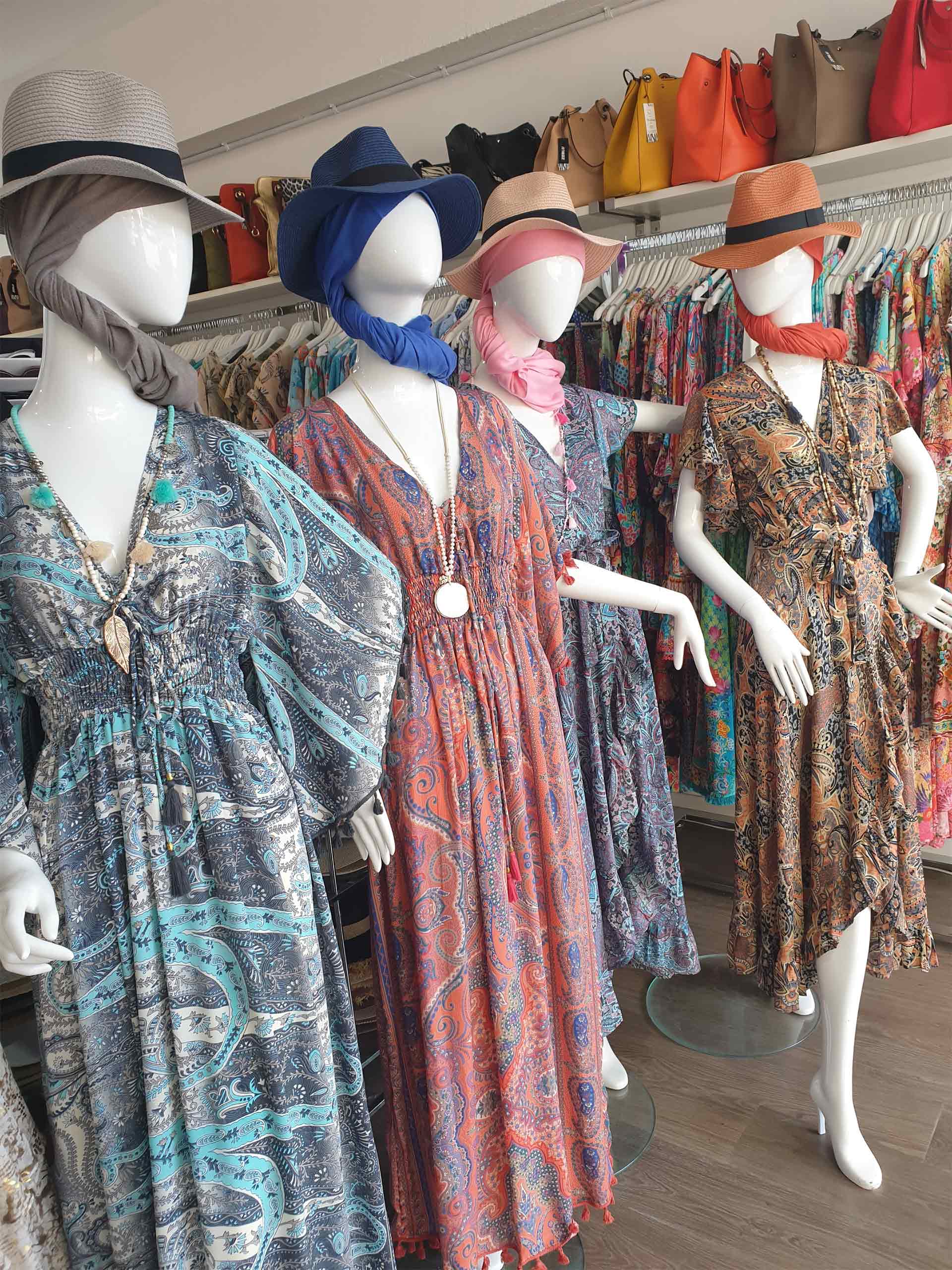 Mannequins in a clothing store display colorful summer dresses and hats.