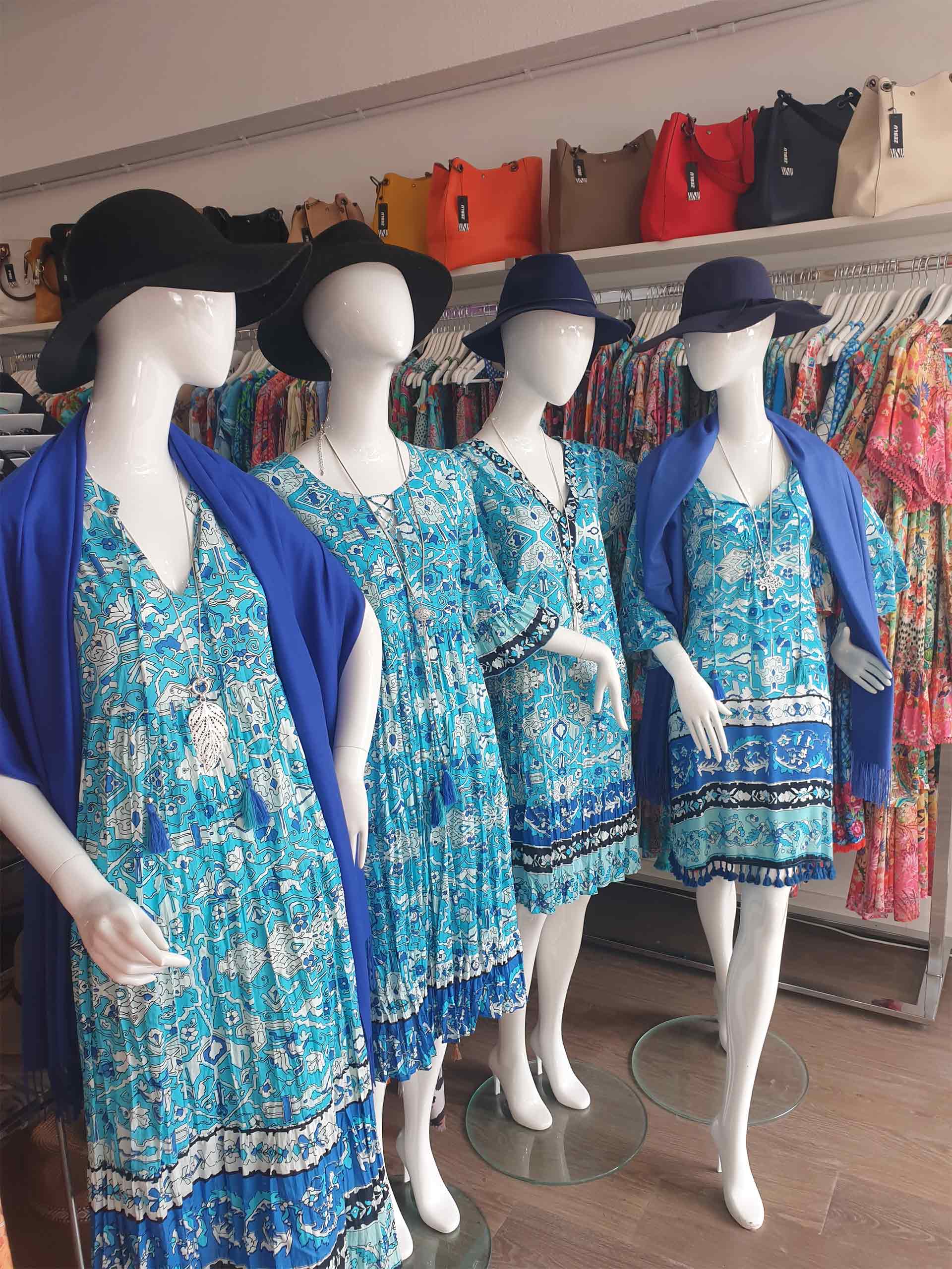 Four mannequins in blue print dresses and hats, inside a clothing store.