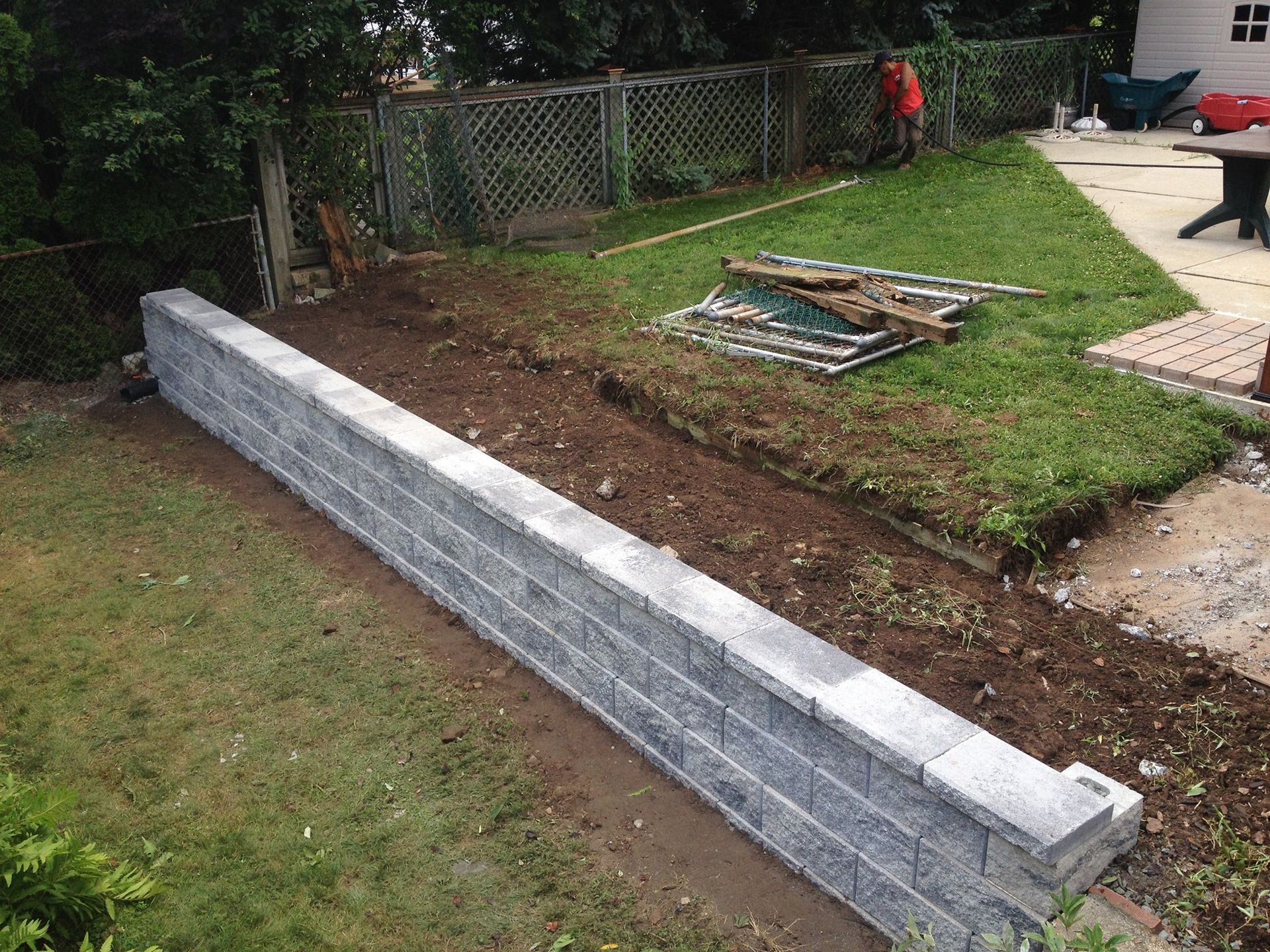 Stone retaining wall being built in a backyard. A person is working in the background.