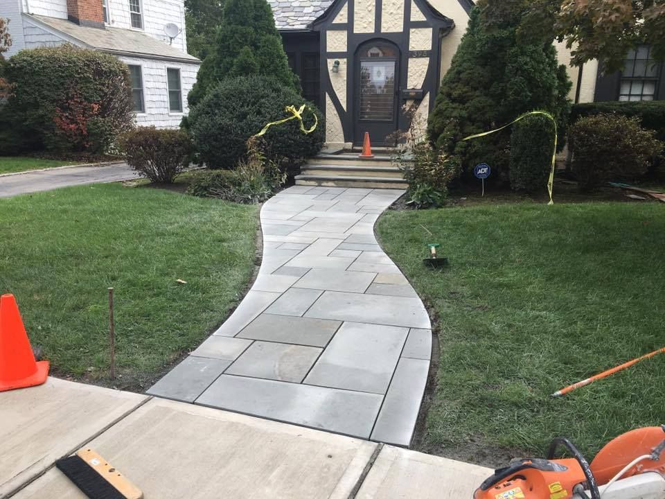 Stone walkway leading to a house with a Tudor-style facade; grass lawn on both sides.