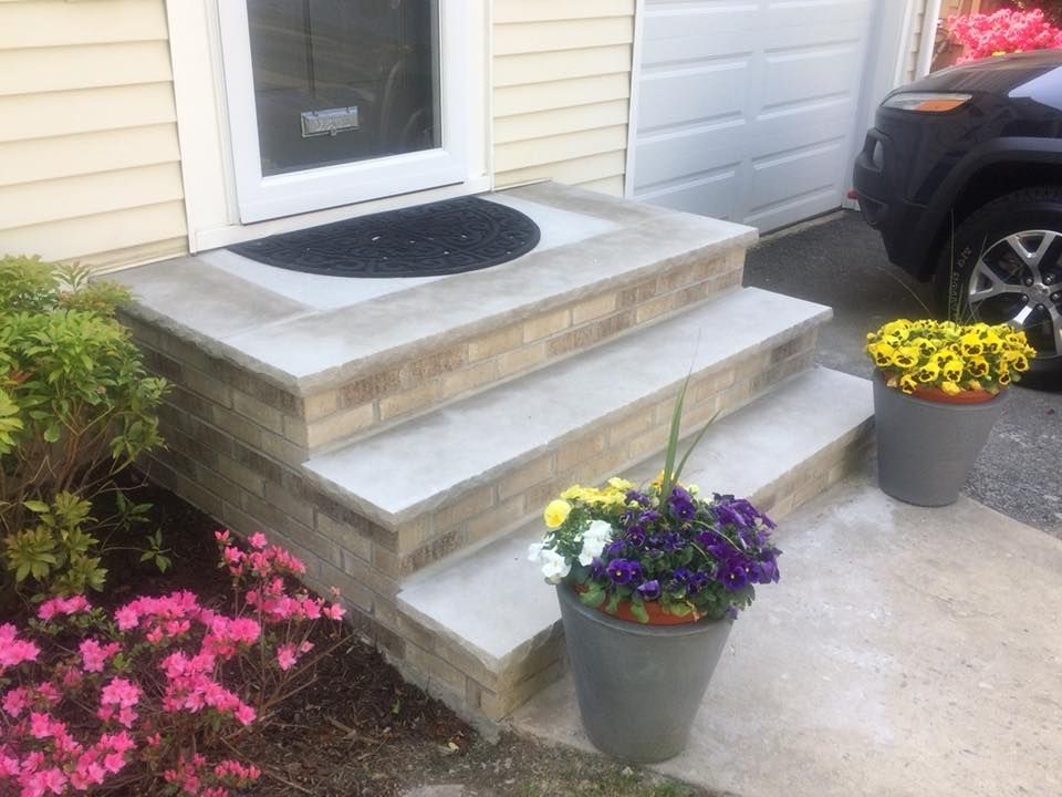 Stone steps leading to a front door, with potted flowers on either side. A car is parked nearby.