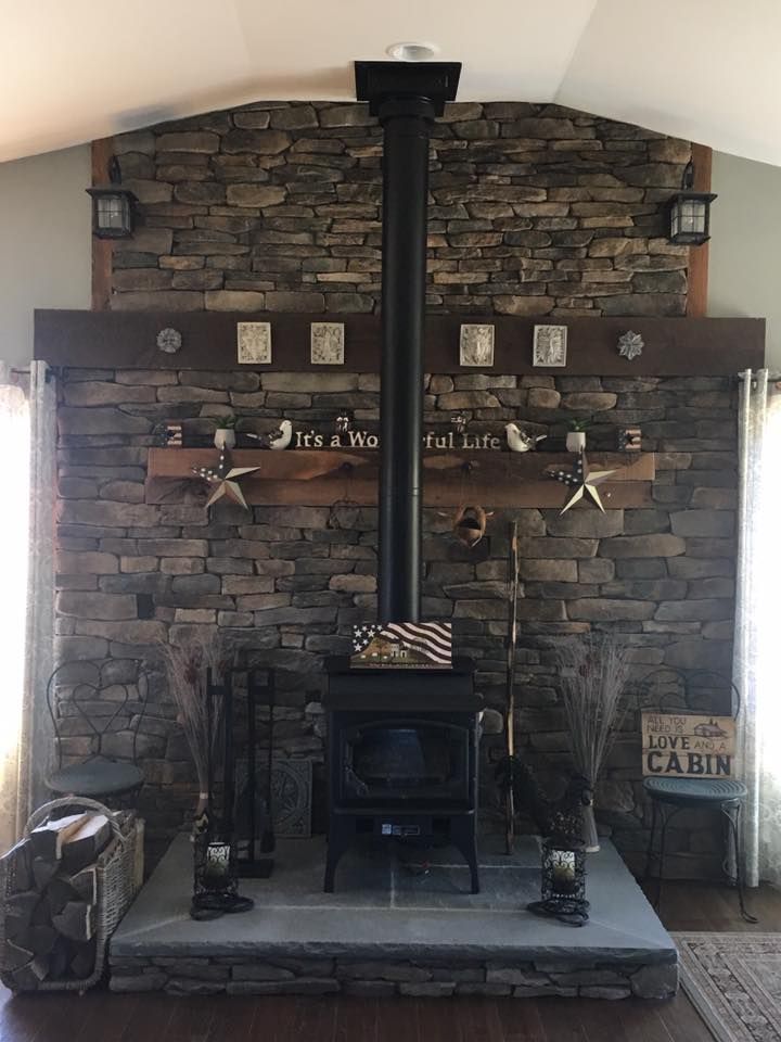 Stone fireplace with wood-burning stove and black chimney, decorated with rustic accents.