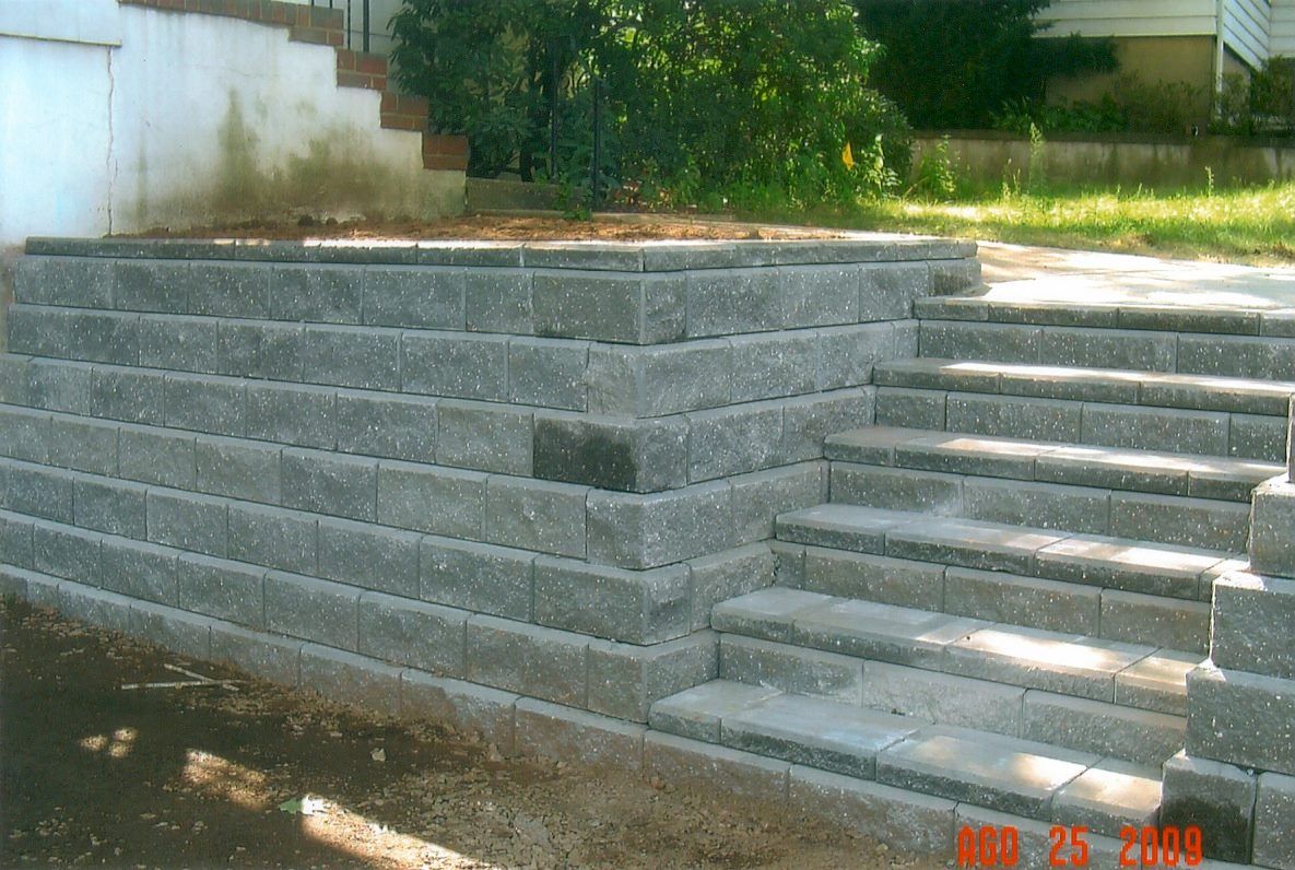 Gray block retaining wall with steps leading up to an elevated area, outdoor setting.
