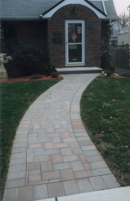Brick pathway leading to a brick house with a front door and small landscaping.