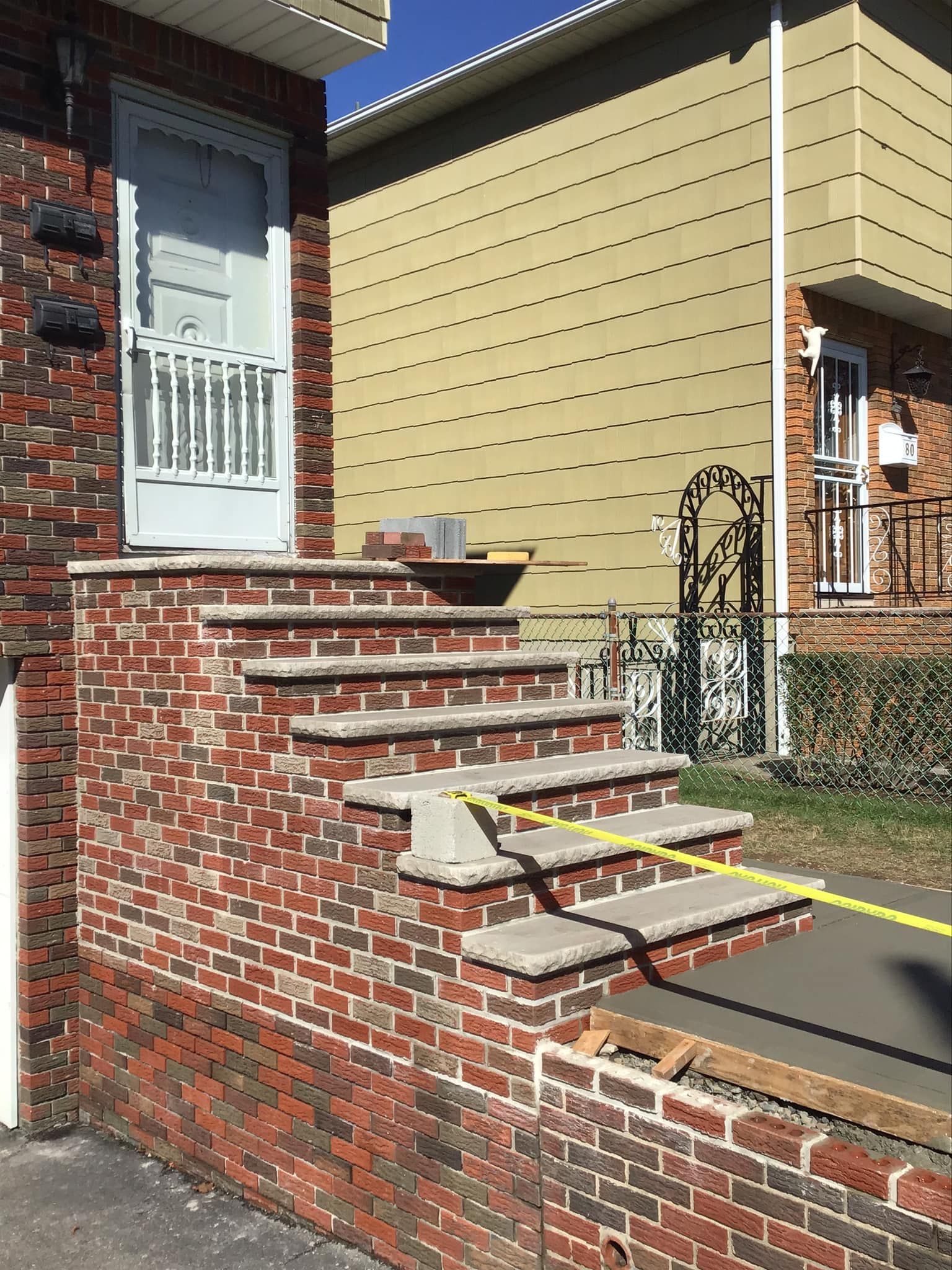 Brick steps leading up to a white door; new concrete work visible with yellow caution tape.