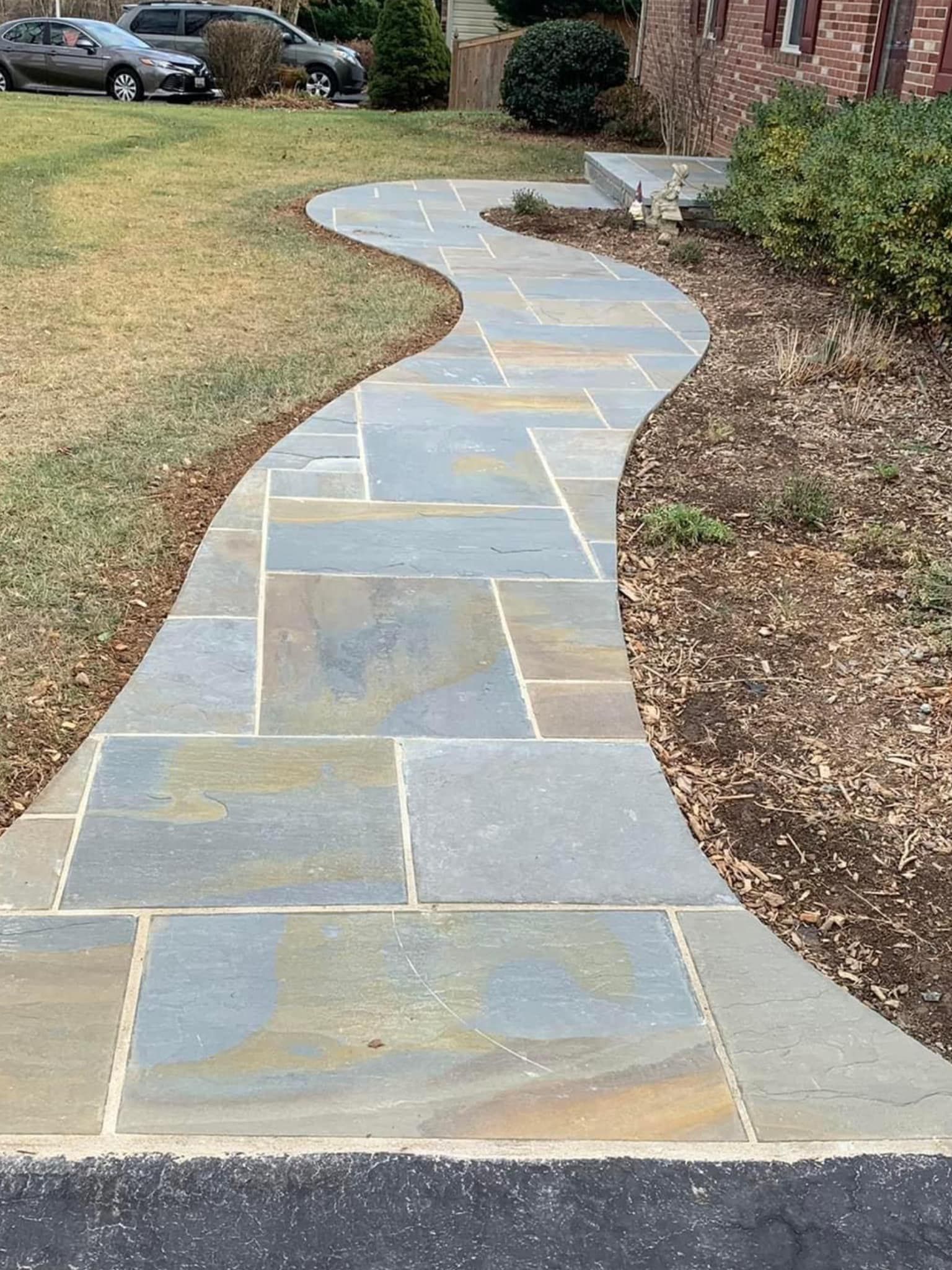 Stone walkway with a wavy design leads to a brick home.