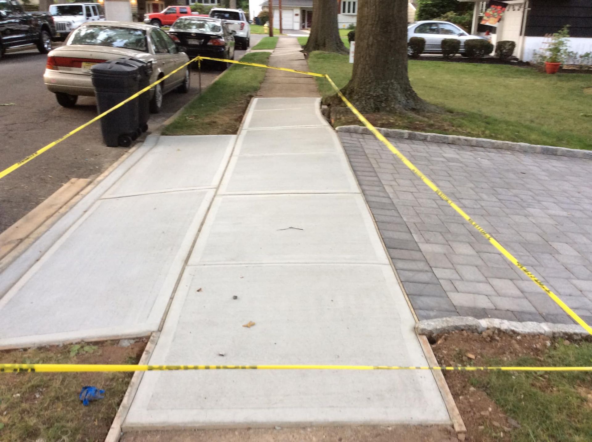 Sidewalk with newly poured concrete, under construction, bordered by yellow caution tape.