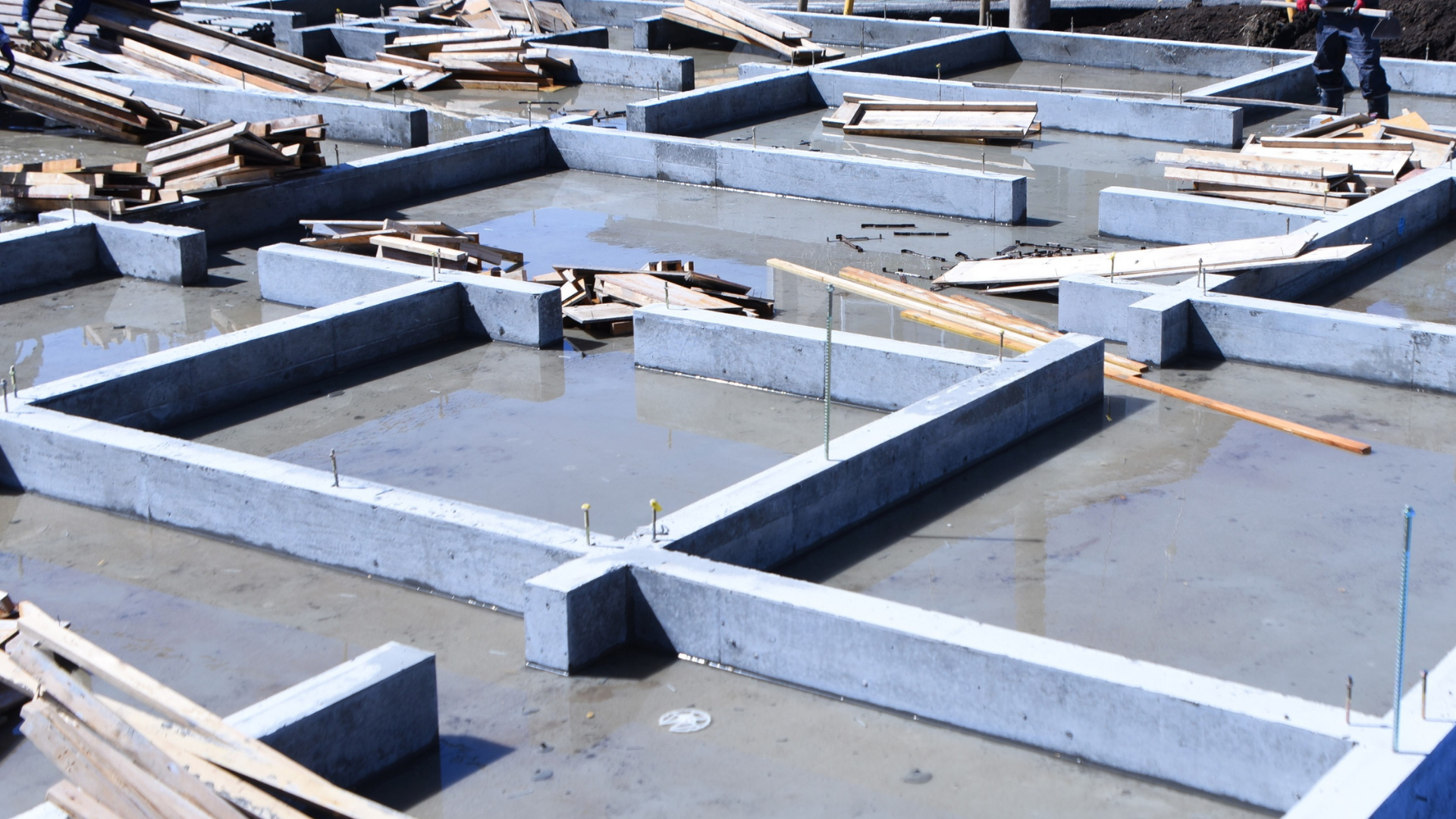 Construction of a retaining wall: worker in safety vest, blocks, drainpipe, dirt, tools, and materials.