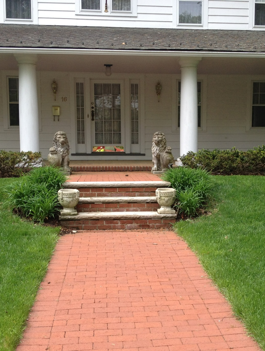 Red brick path leads to the front door of a white house with pillars. Stone lions flank the entrance.
