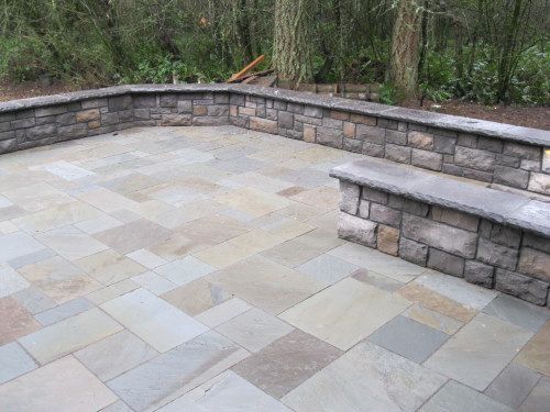 Stone patio with low stone walls and benches, surrounded by trees.