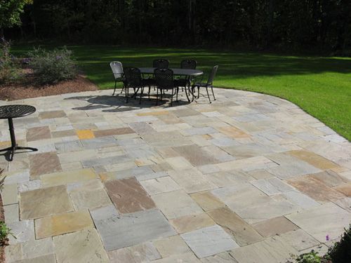 Patio paved with varied stone slabs, with black table and chairs, and a smaller side table on grass.