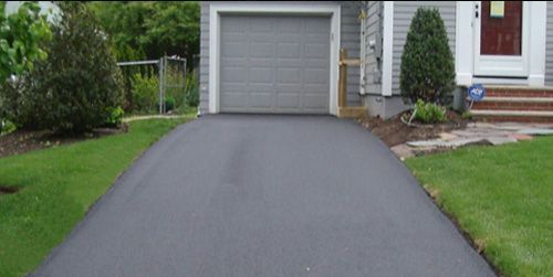 Paved driveway leading up to a gray garage door, with green grass on either side.