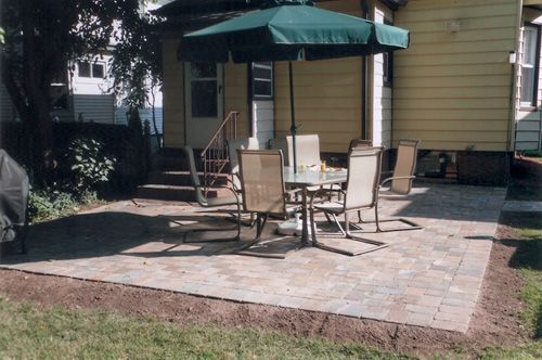 Patio with table, chairs, and umbrella in a backyard next to a yellow house.