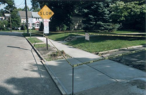 New concrete sidewalk with caution tape, street sign.