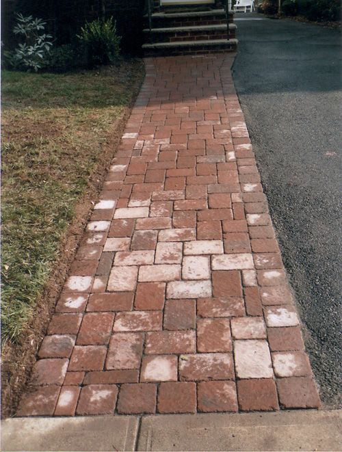 Brick pathway leading to steps, bordered by grass and asphalt.