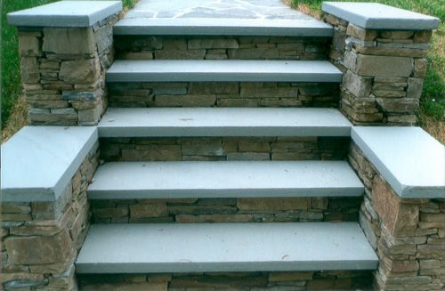 Stone steps with gray treads, flanked by stone walls, lead upwards.