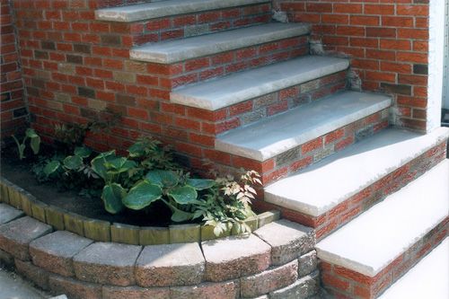 Brick steps with concrete treads, built-in flower bed with green plants, and red brick wall.