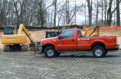 Red pickup truck parked near construction equipment and a dirt pile.