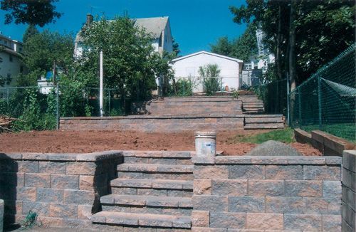 Stone retaining walls with steps leading up a sloped yard.