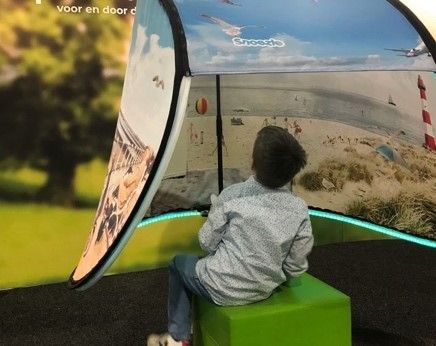 A young boy is sitting on a green cube in front of a large Snoezle screen.
