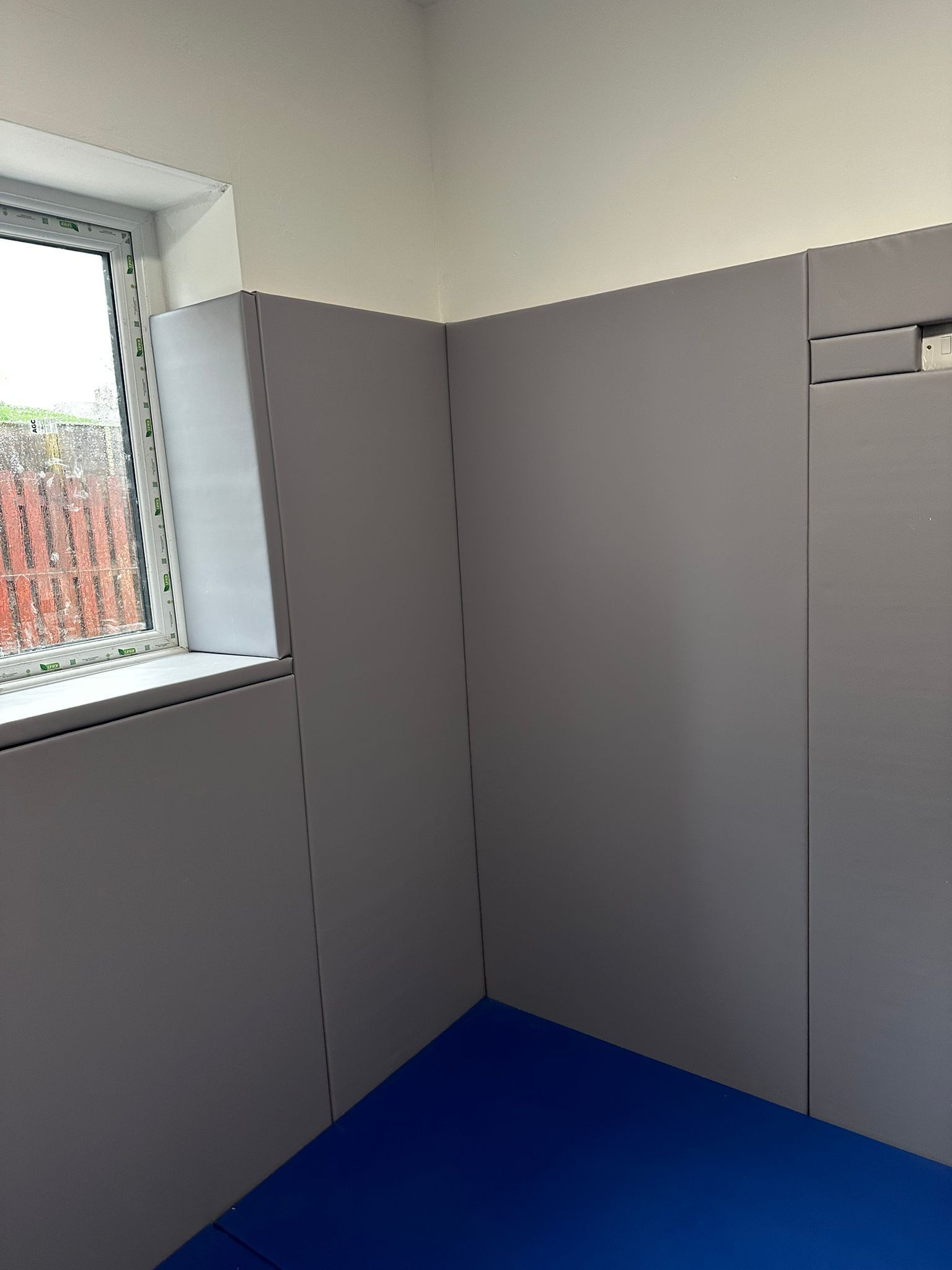 room with a window, a blue padded floor and grey padded walls