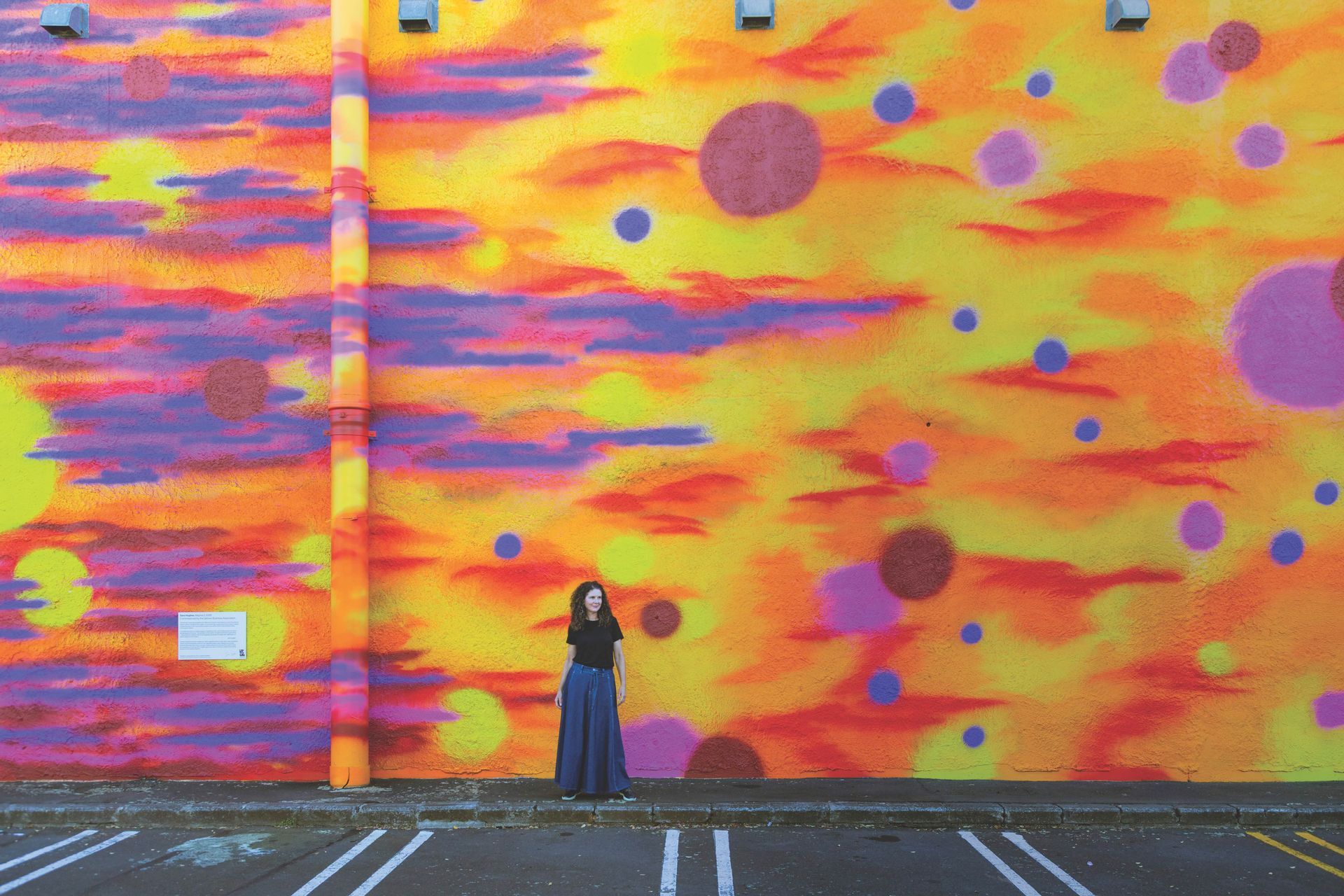 A woman is standing in front of a colorful wall in a parking lot.