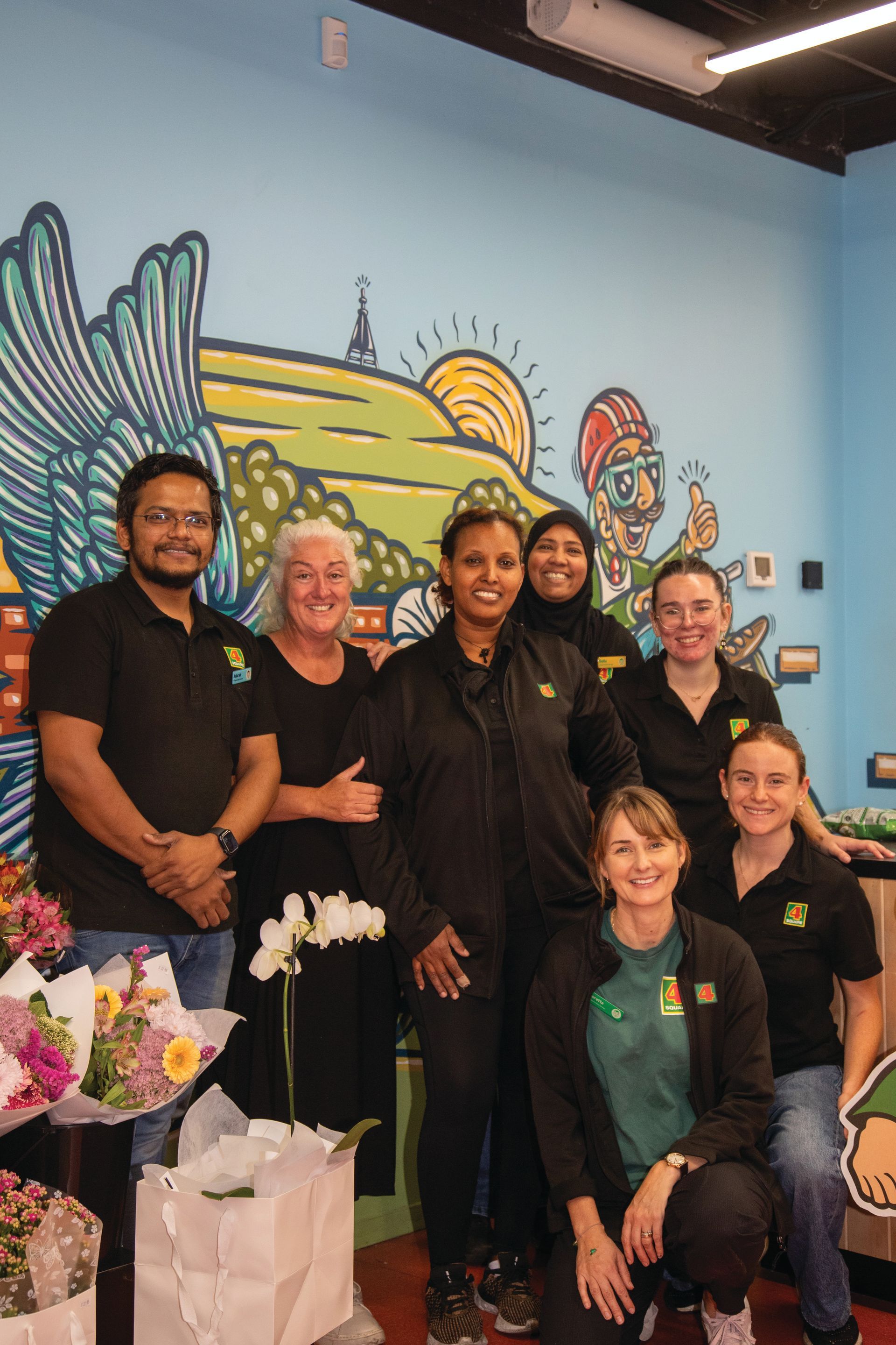 A group of people are posing for a picture in front of a mural.