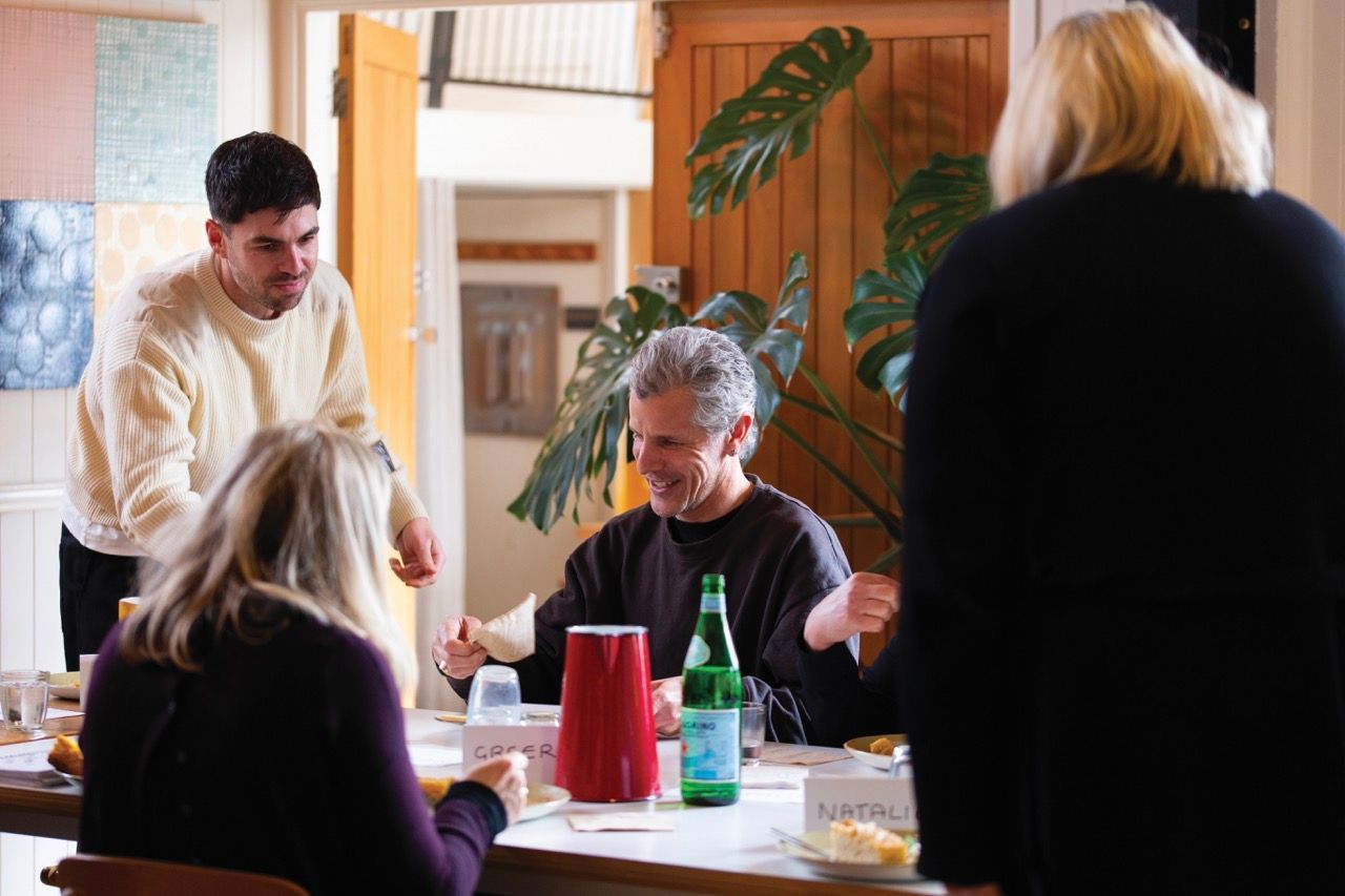 People gathered around a table. Light, airy room with artwork and plants.